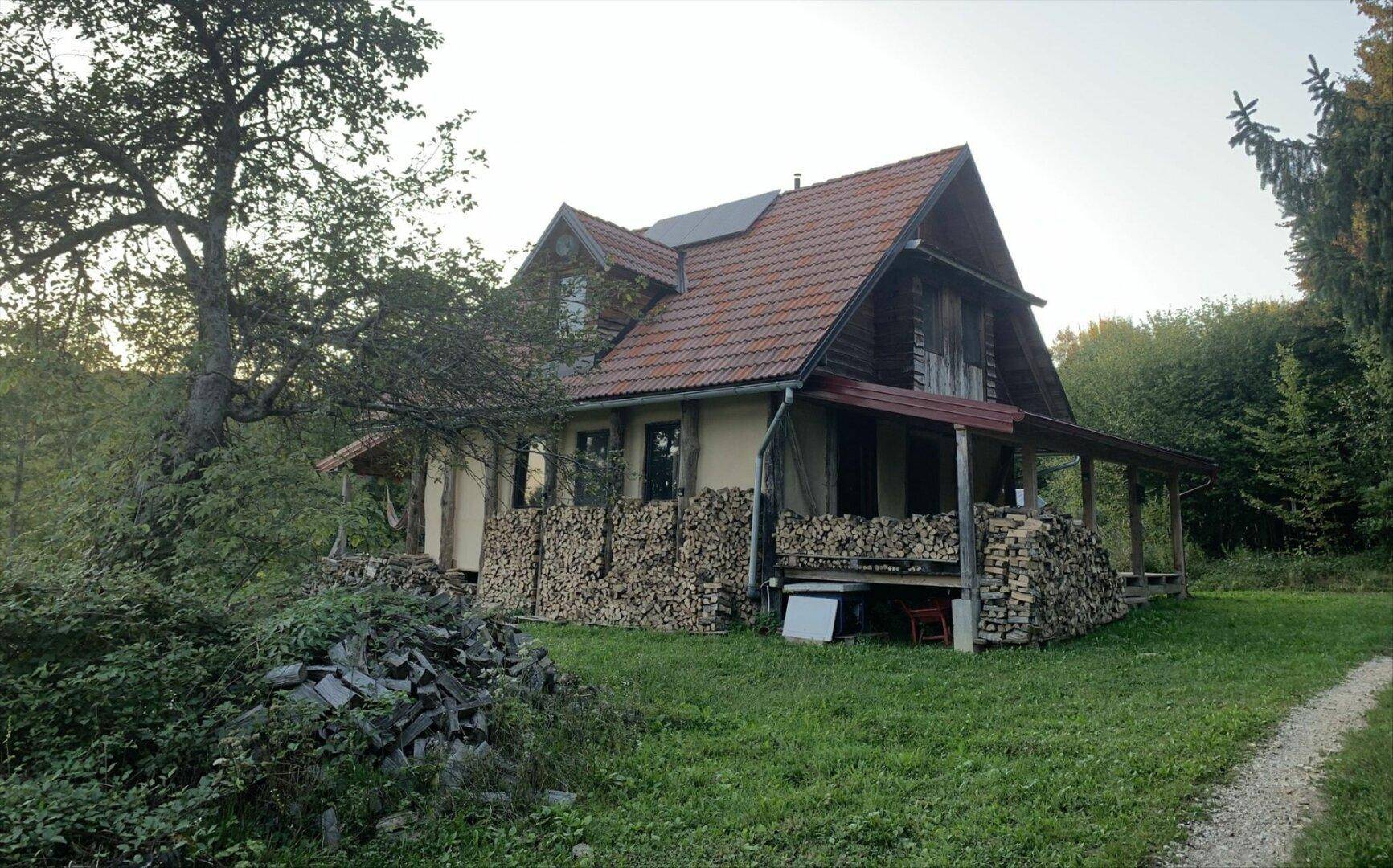Rustikales Haus mit Holzstapeln an der Fassade und umgeben von Bäumen.