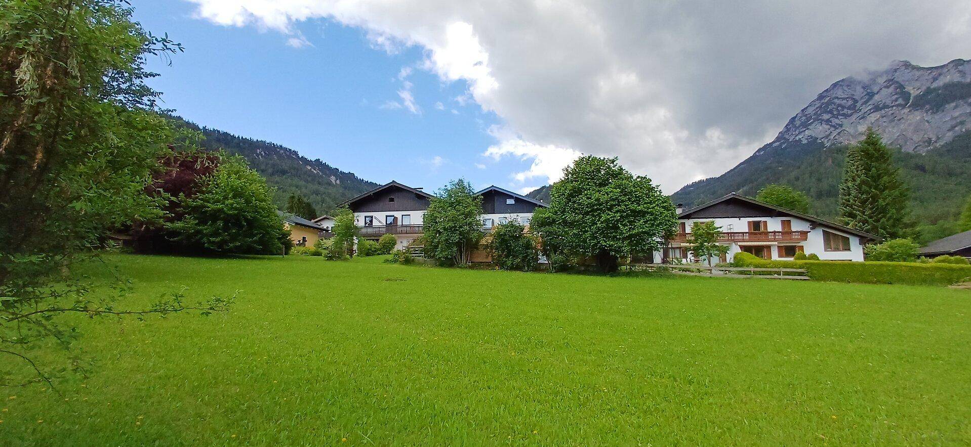 Reihe von Häusern mit traditioneller Architektur, umgeben von weiten Rasenflächen und Bergen.