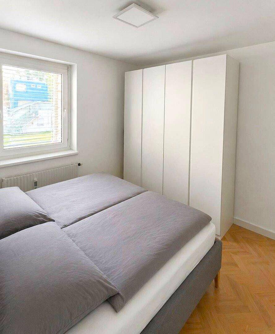 Helles Schlafzimmer mit großem Kleiderschrank, Doppelbett und Fenster.