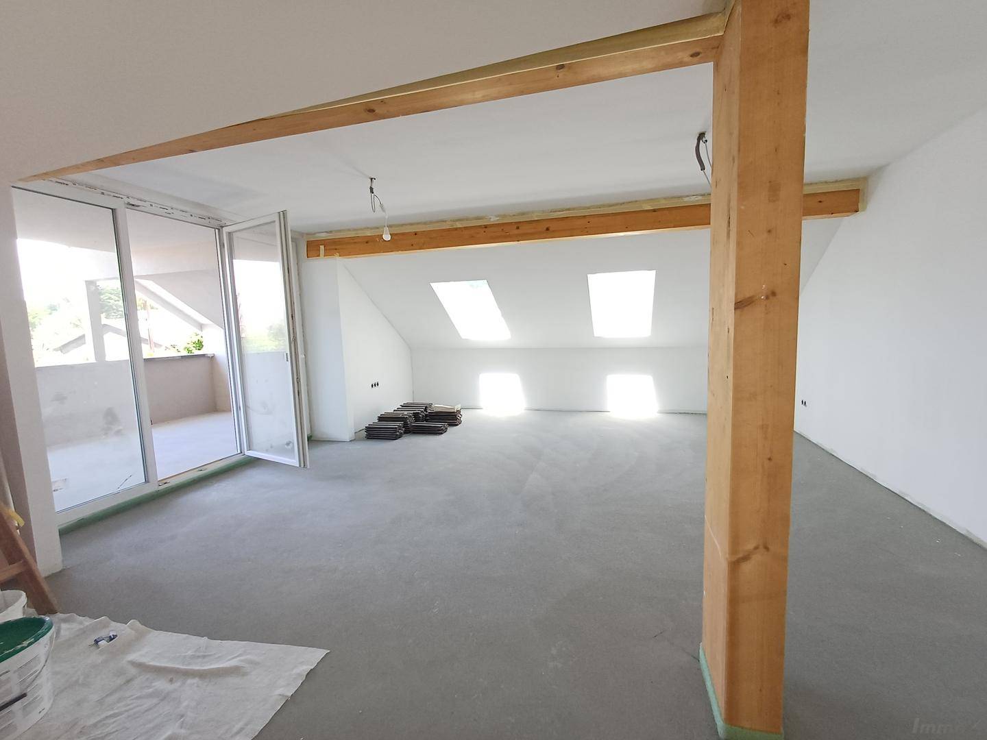 Geräumiger, unfertiger Dachgeschossraum mit sichtbaren Holzbalken und viel Tageslicht durch die Fenster.