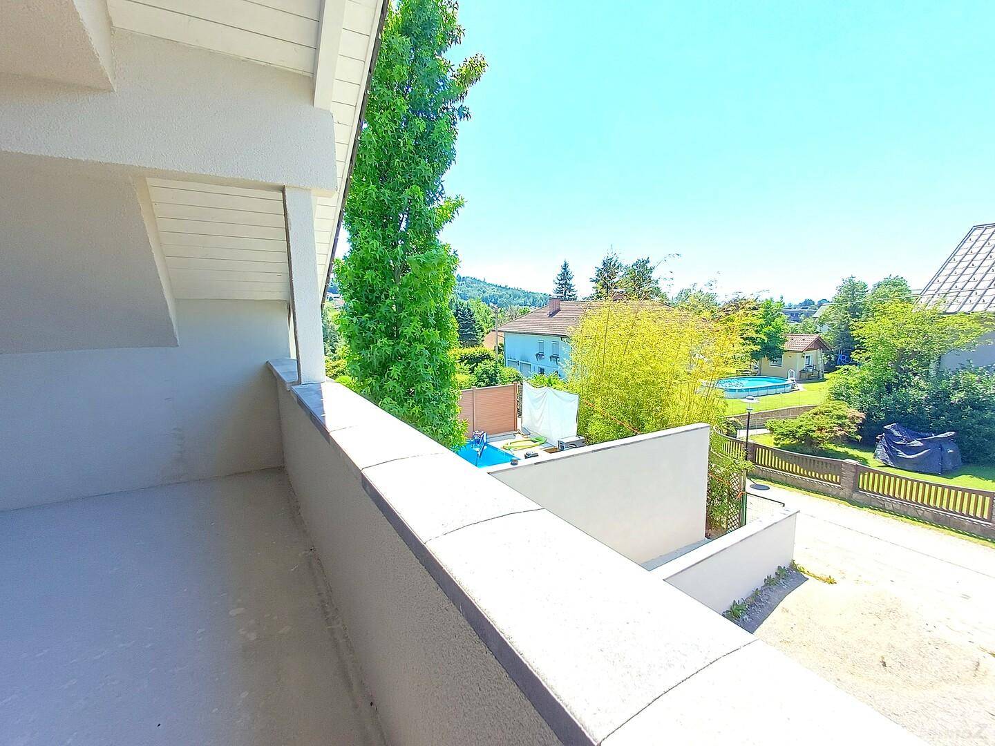 Geräumiger Balkon mit Blick auf die umliegende Wohngegend und viel Grün unter strahlendem Himmel.