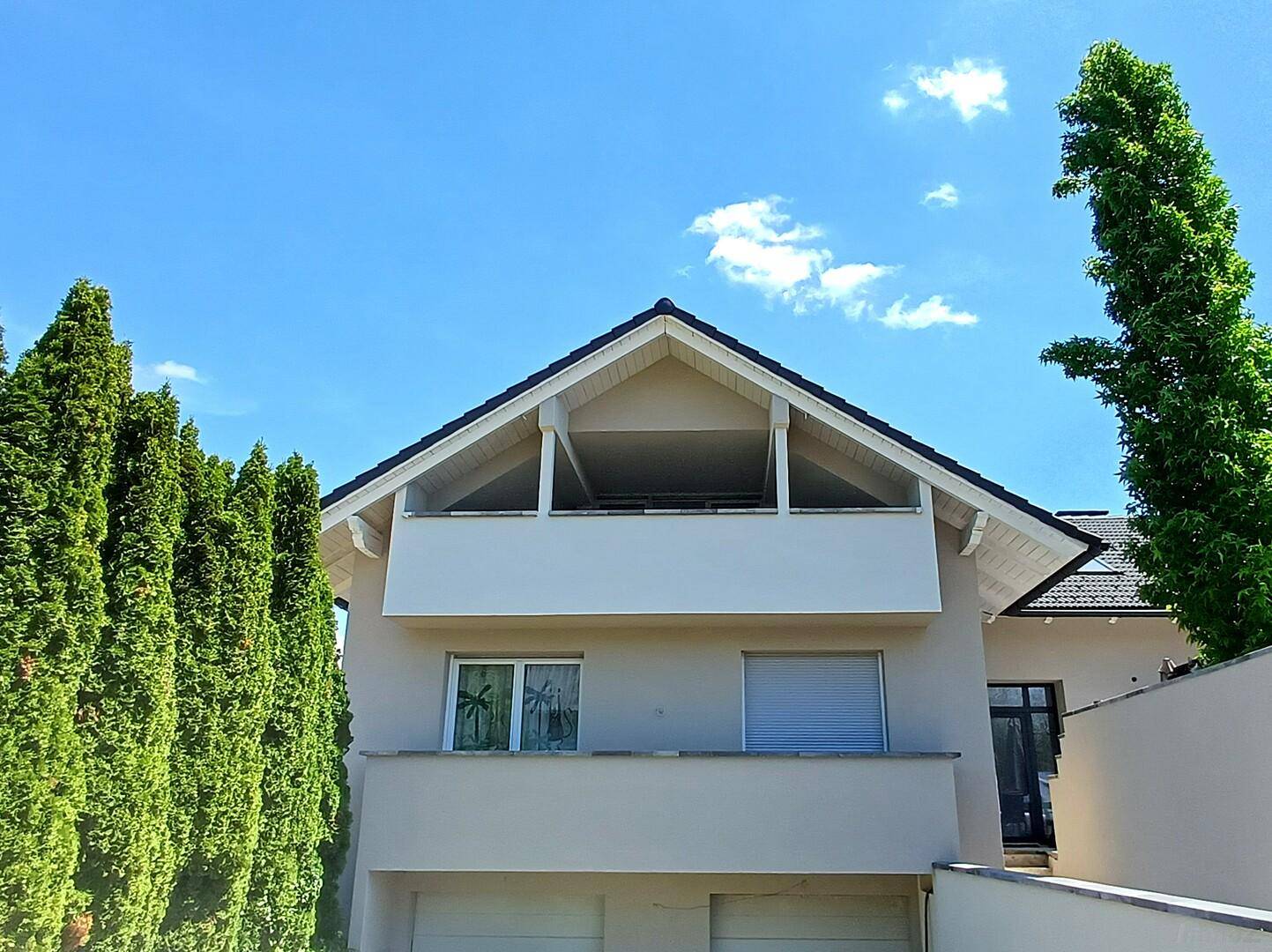 Modernes Einfamilienhaus mit Satteldach, Balkon und integrierter Doppelgarage unter blauem Himmel.