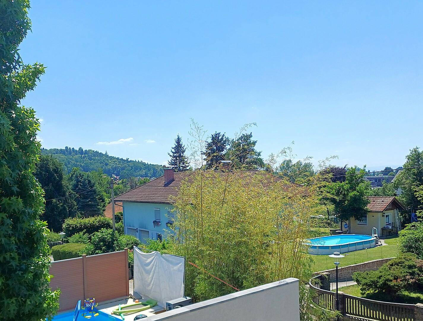 Blick über die Nachbarschaft mit Häusern, Bäumen und einem Pool im Garten. Hügel sind in der Ferne sichtbar.