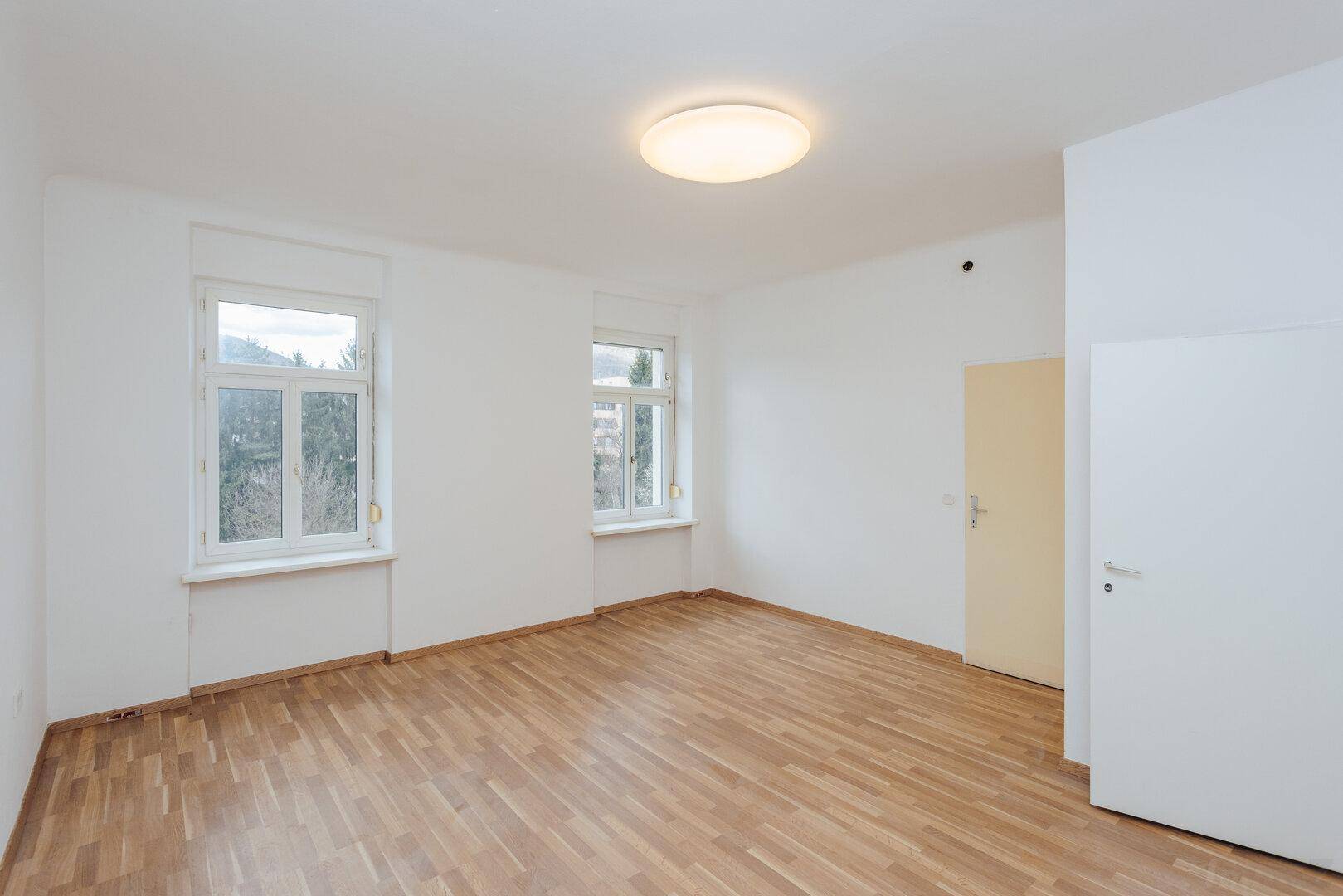 Heller Raum mit Parkettboden, weißen Wänden und einer Tür, bereit zur individuellen Gestaltung.
