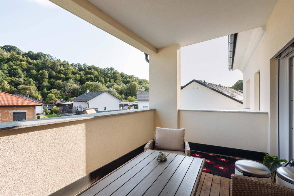 Sonniger Balkon mit Holzboden und weitem Blick auf die grüne Hügellandschaft.