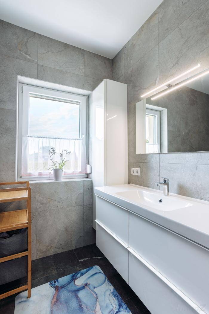 Helles Badezimmer mit modernem Waschtisch, Spiegel und Fenster für natürliche Belüftung.