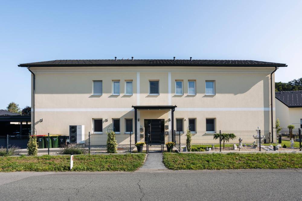 Moderne Gebäudefassade mit hellem Anstrich, vielen Fenstern und gepflegtem Vorgarten.