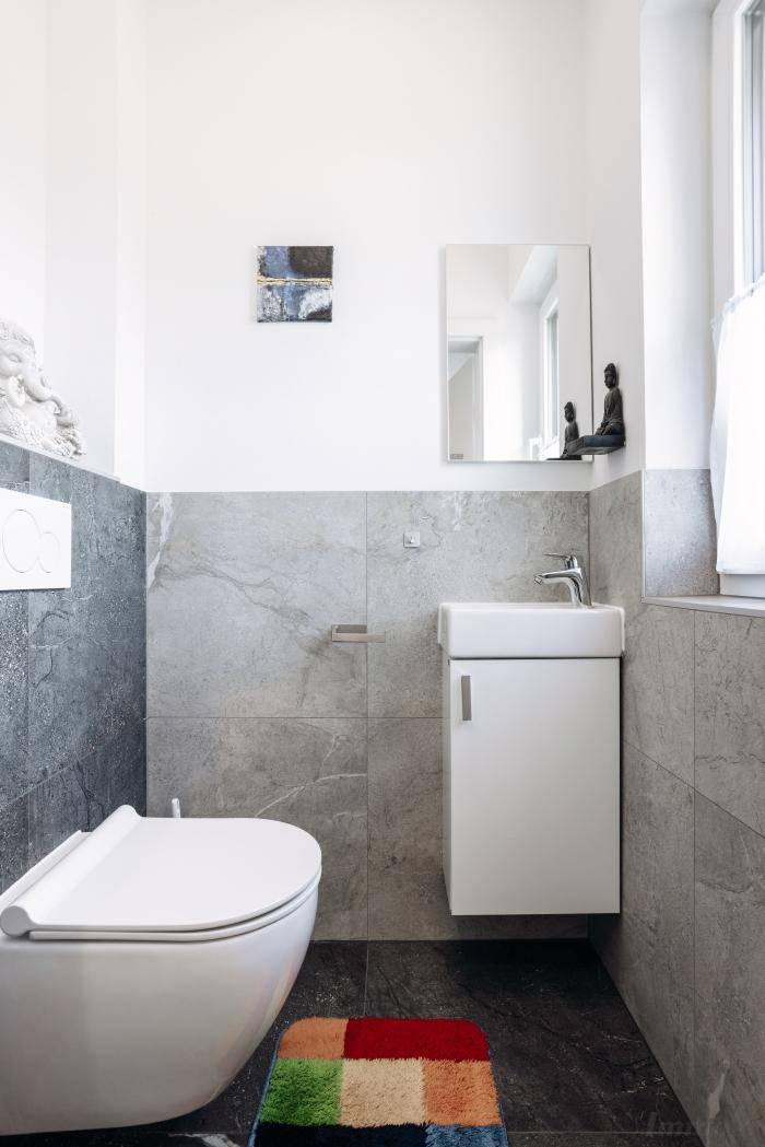 Separates WC mit wandhängender Toilette, kleinem Waschbecken und modernen Fliesen.