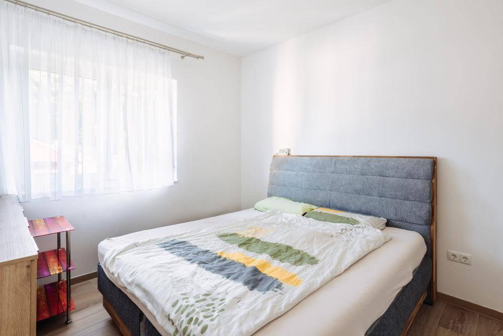 Schlafzimmer mit Doppelbett, schlichtem Kopfteil und großem Fenster für viel Tageslicht.