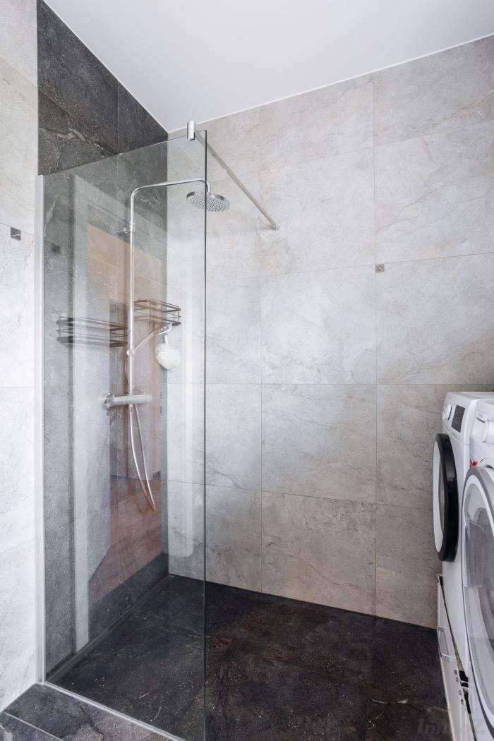 Modernes Badezimmer mit begehbarer Dusche, grauen Fliesen und integrierter Waschmaschine.