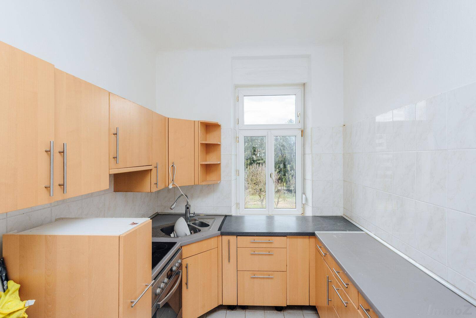 Funktionale Küche mit hellen Holzschränken, dunkler Arbeitsplatte und Fenster mit Blick ins Grüne.