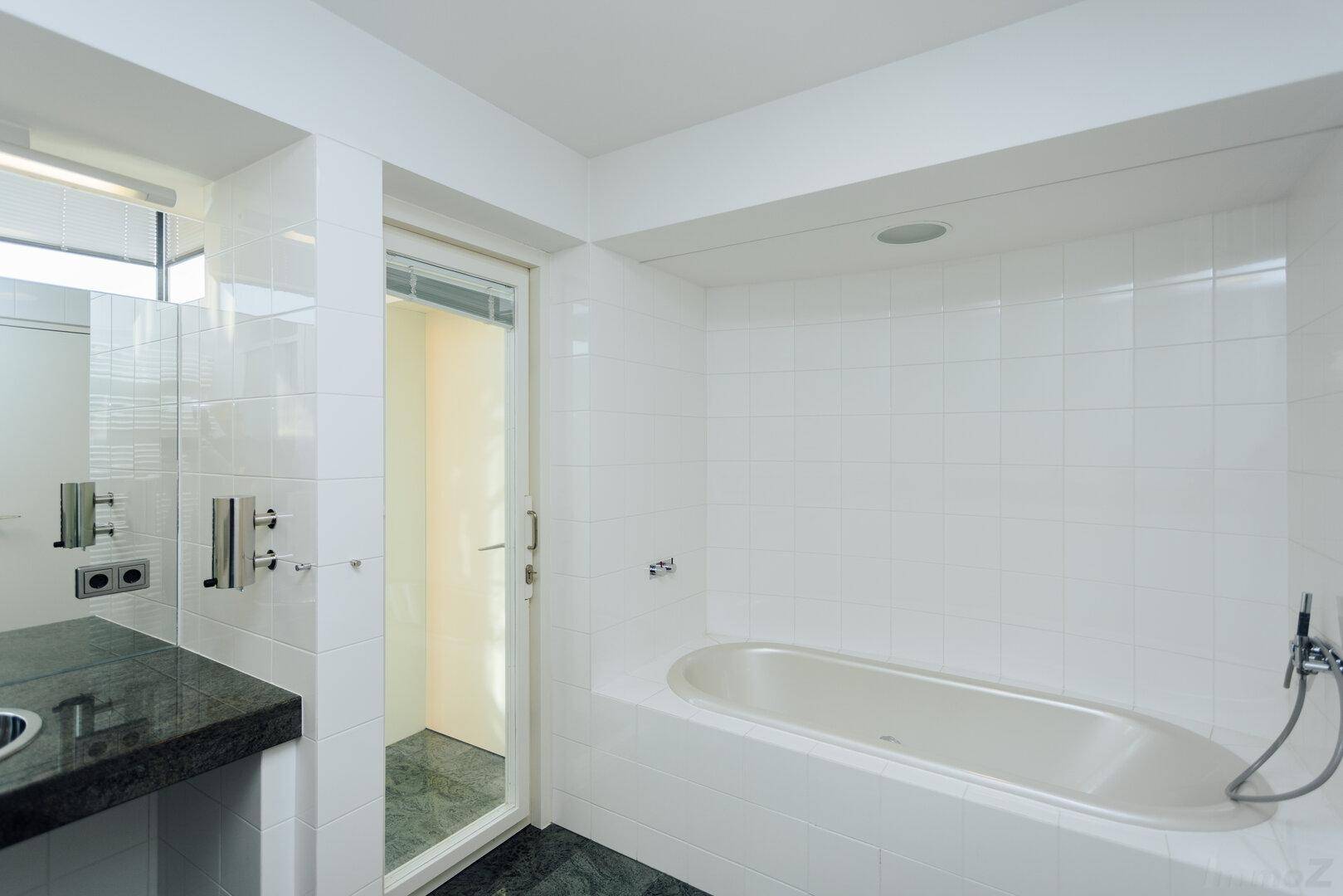 Helles Badezimmer mit Badewanne, Dusche und dunkler Granit-Arbeitsplatte.