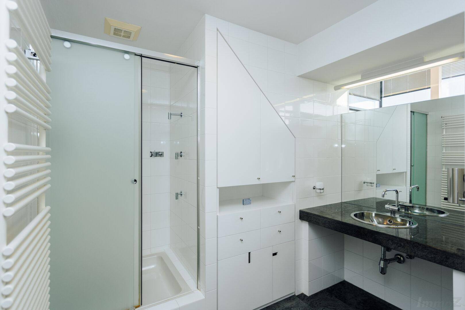 Modernes Badezimmer mit Doppelwaschbecken, großer Dusche und Spiegelschrank.