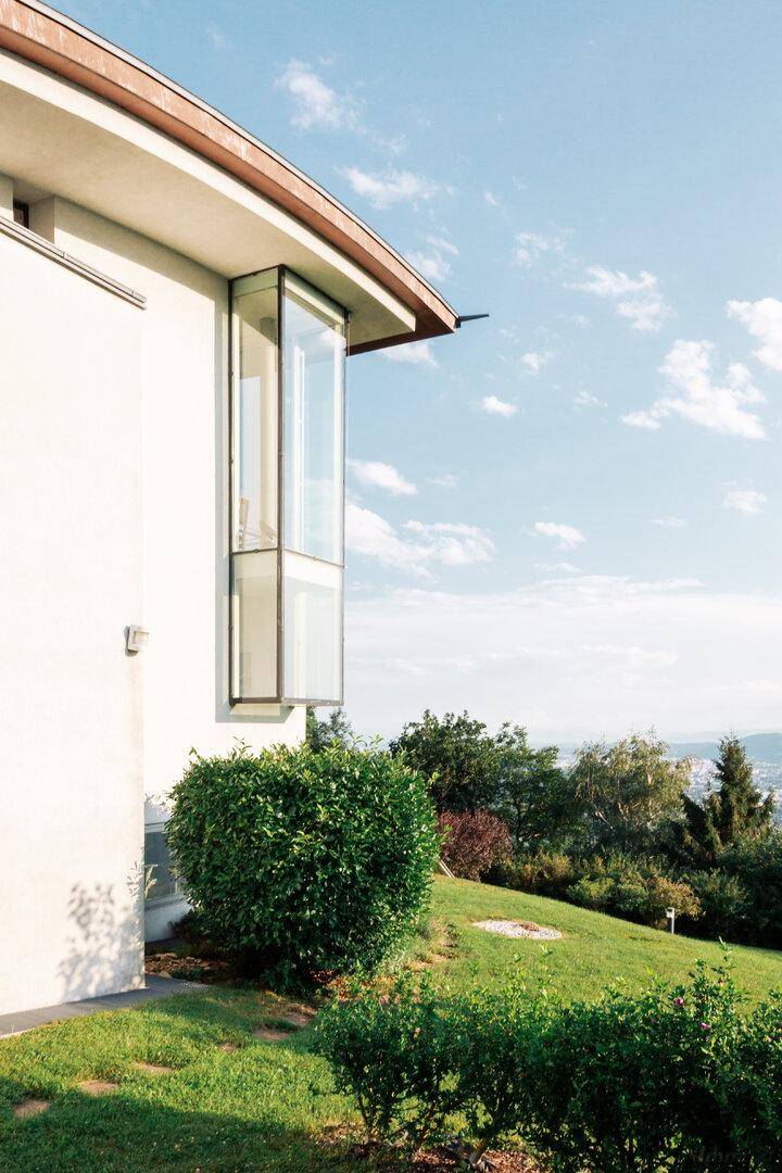 Seitenansicht eines modernen Hauses mit Erkerfenster und weitem Blick in die grüne Landschaft.