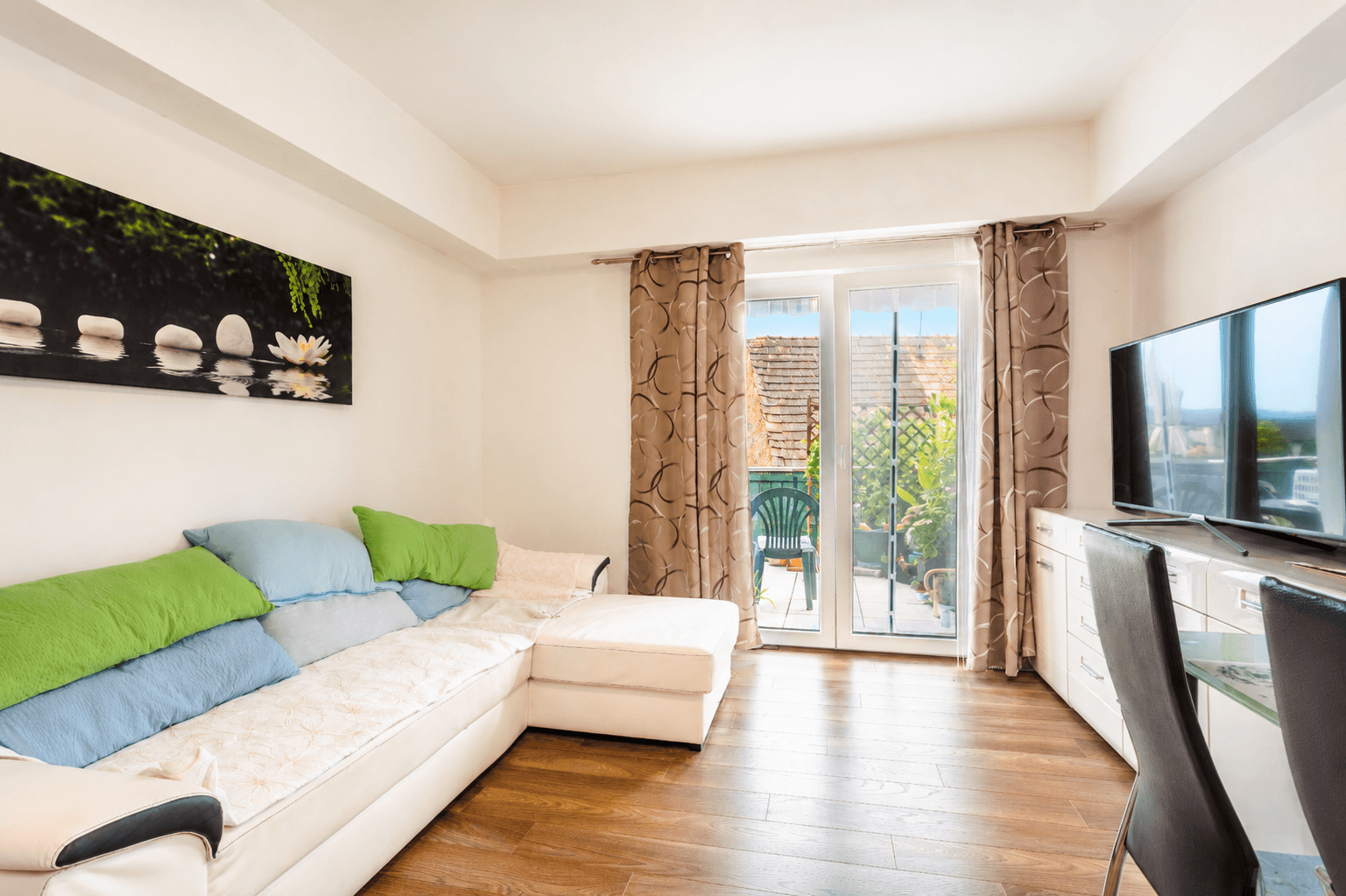 Gemütliches Wohnzimmer mit Sofa, Fernseher und Zugang zu einem kleinen Balkon oder einer Terrasse.
