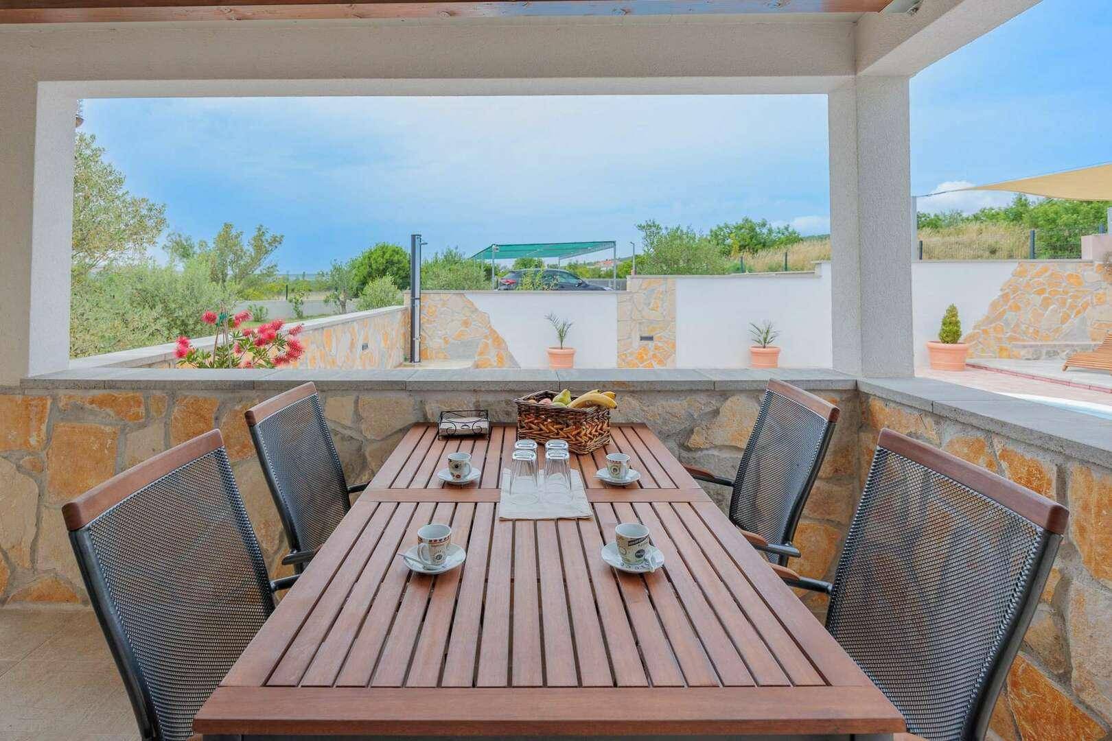 Überdachte Terrasse mit Esstisch und Stühlen, ideal für Mahlzeiten im Freien mit Blick ins Grüne.