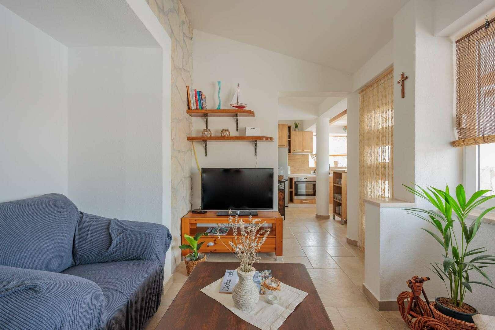 Helles Wohnzimmer mit Sofa, Fernseher und Blick auf den angrenzenden Küchenbereich.