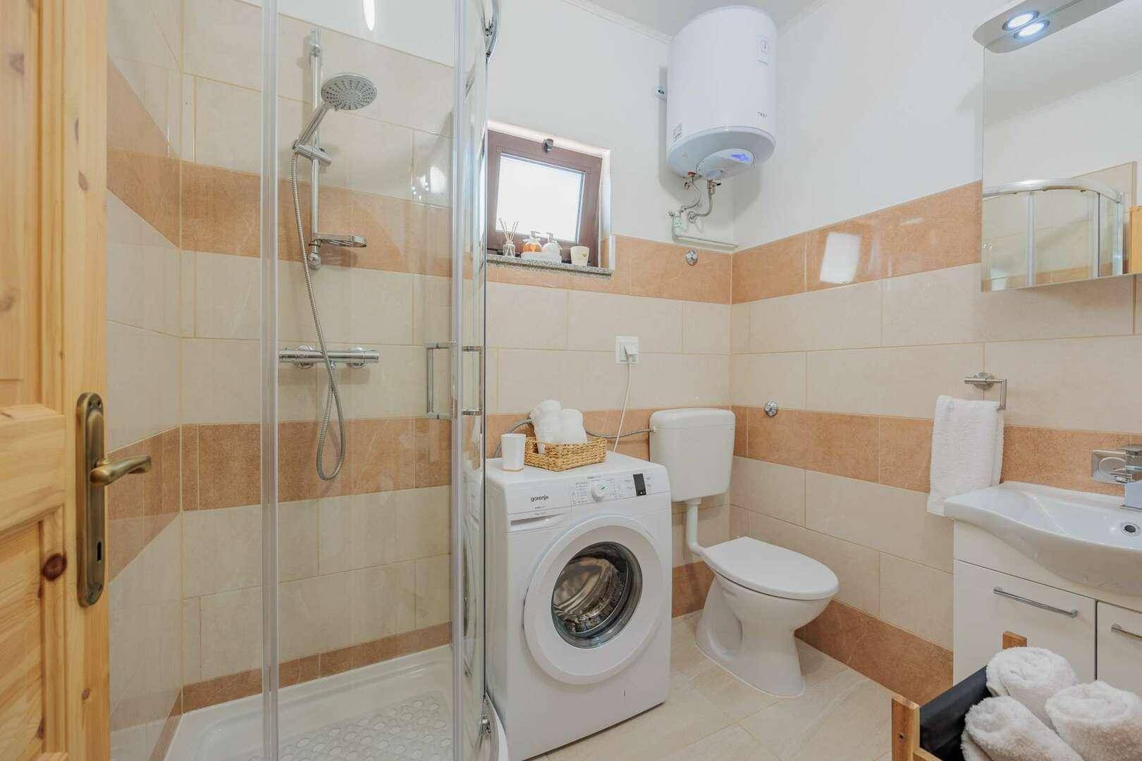 Funktionales Badezimmer mit Duschkabine, WC, Waschbecken und einer Waschmaschine.