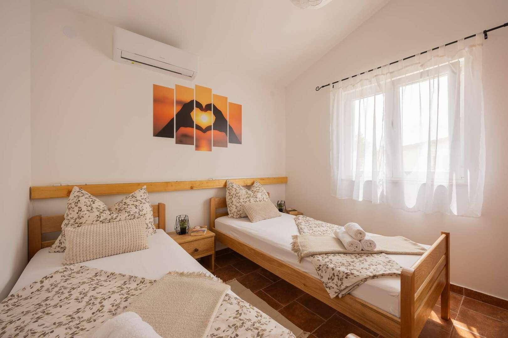 Helles Schlafzimmer mit zwei Einzelbetten, Klimaanlage und dekorativen Wandbildern.
