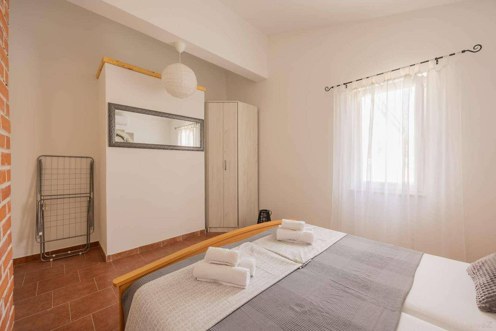 Helles Schlafzimmer mit Doppelbett, Kleiderschrank und einem großen Spiegel an der Wand.