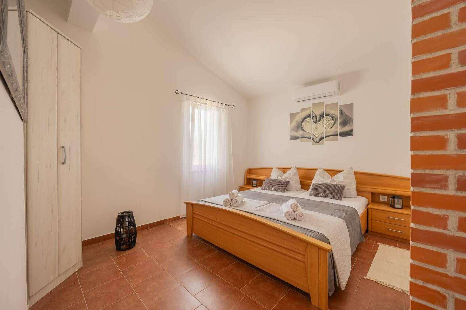 Gemütliches Schlafzimmer mit Doppelbett, Holzmöbeln, Klimaanlage und Terrakotta-Fliesenboden.