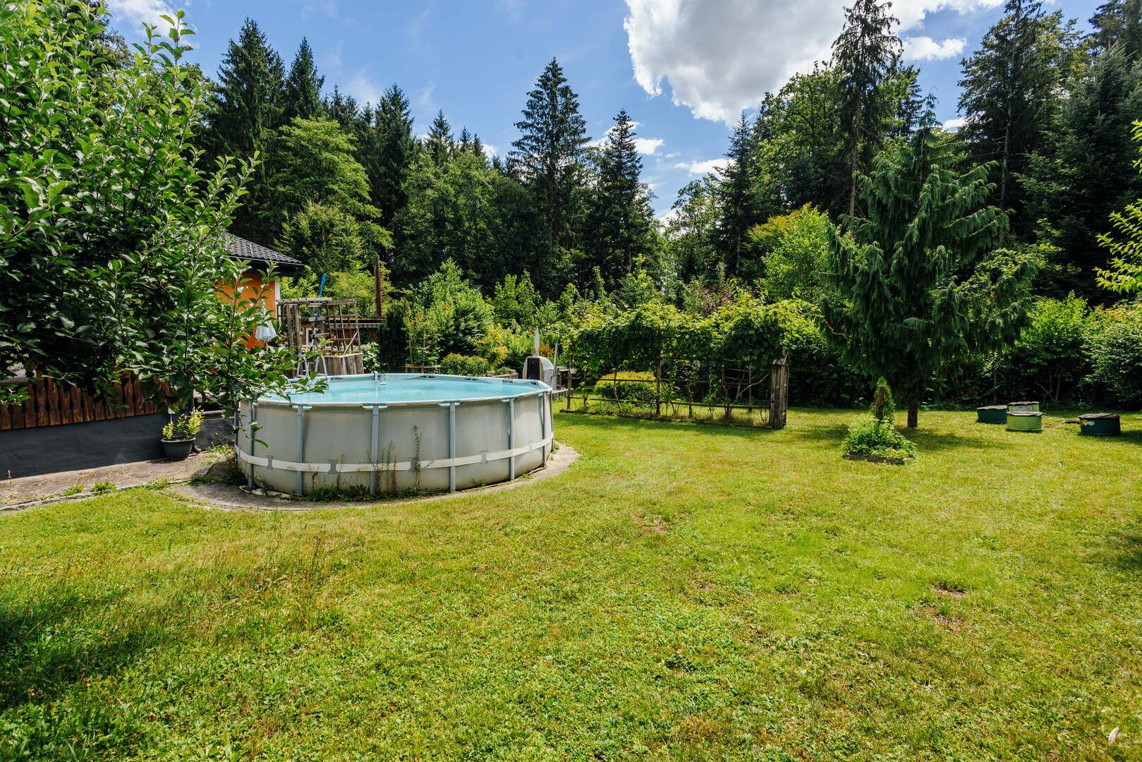 Großer Gartenbereich mit einem Aufstellpool, umgeben von Rasen und Bäumen.