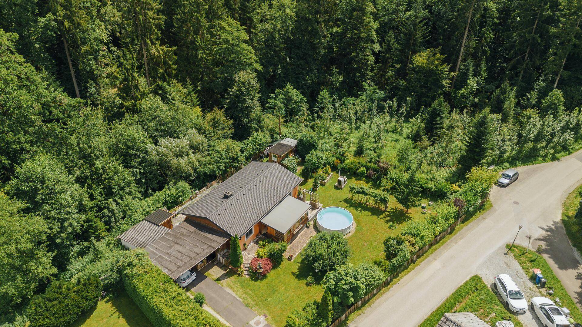 Luftaufnahme des Anwesens mit Haus, Garten, Pool und angrenzendem Waldgebiet sowie Zufahrtsstraße.
