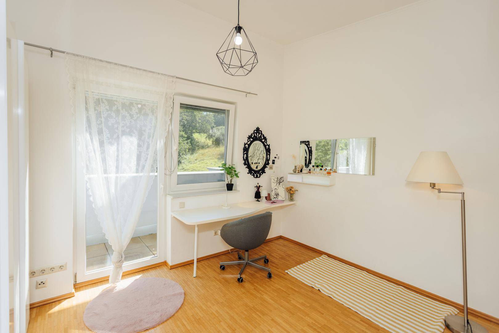 Helles Schlafzimmer mit Holzboden, Schreibtisch und Zugang zu einem französischen Balkon.