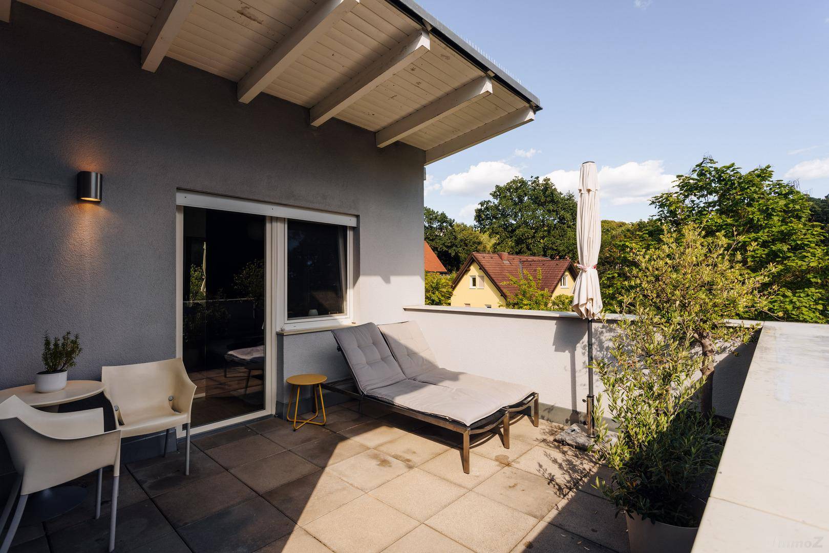 Sonnige Dachterrasse mit Liegestuhl und Sitzgelegenheiten, umgeben von viel Grün.