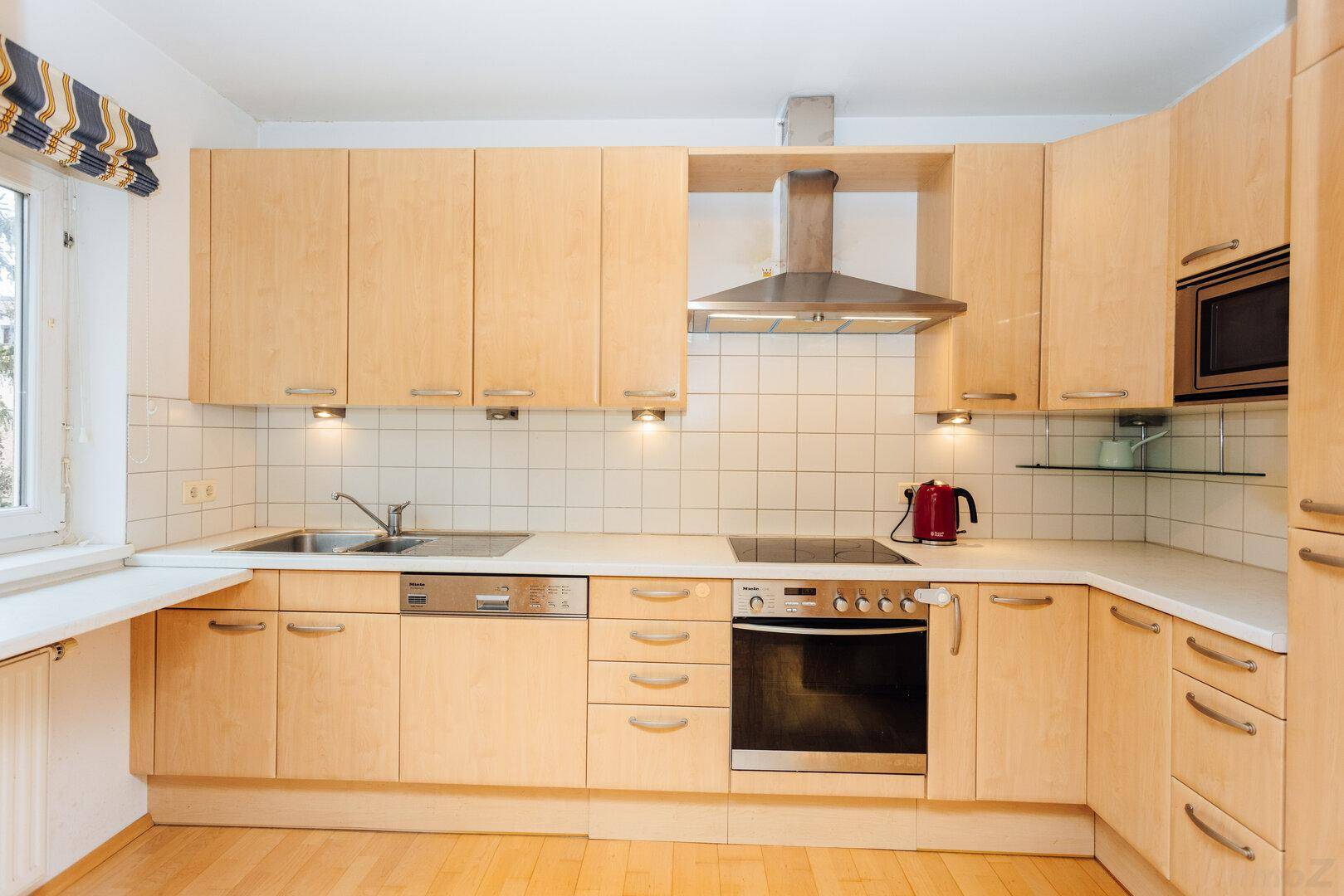 Funktionale Küche mit hellen Holzschränken, Einbaugeräten und Fenster.