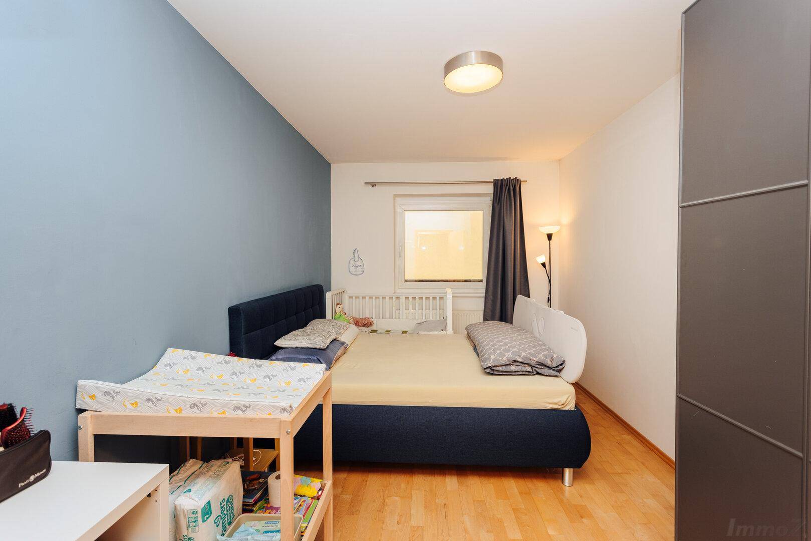 Schlafzimmer mit blauer Akzentwand, Holzboden und Kinderbett.