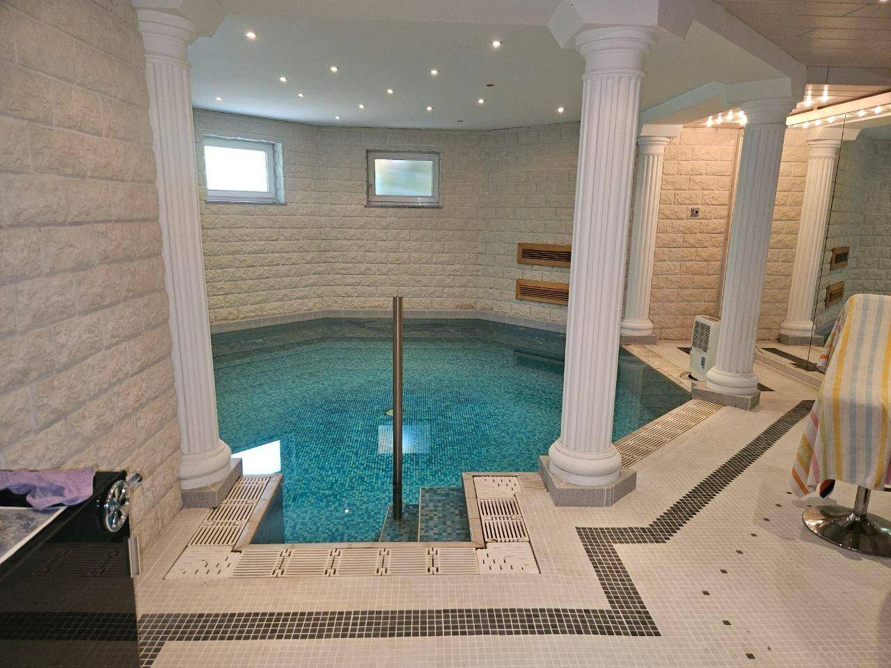 Exklusiver Innenpool mit Säulen und Mosaikfliesen, umgeben von hellen Steinwänden.
