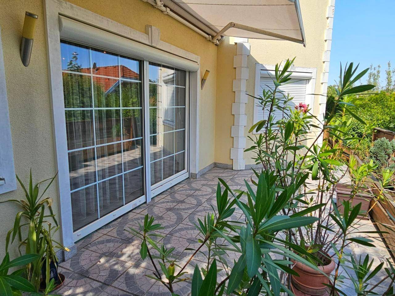 Geflieste Terrasse mit großen Schiebetüren und Markise, umgeben von Topfpflanzen.