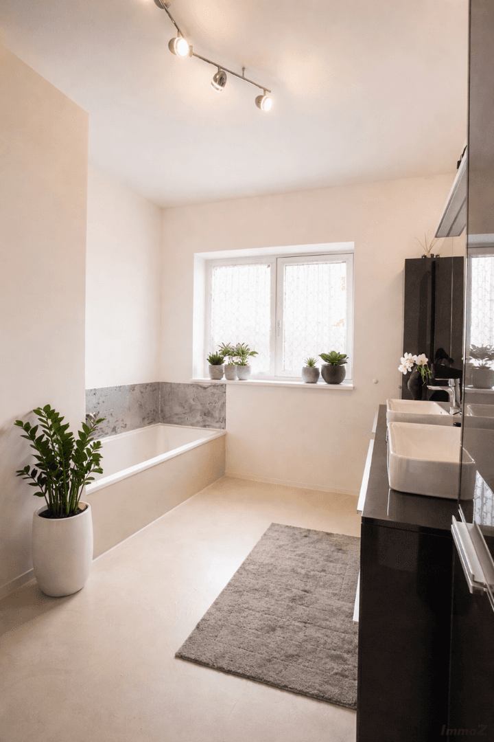 Helles Badezimmer mit Badewanne, Doppelwaschbecken und einem Fenster für Tageslicht.