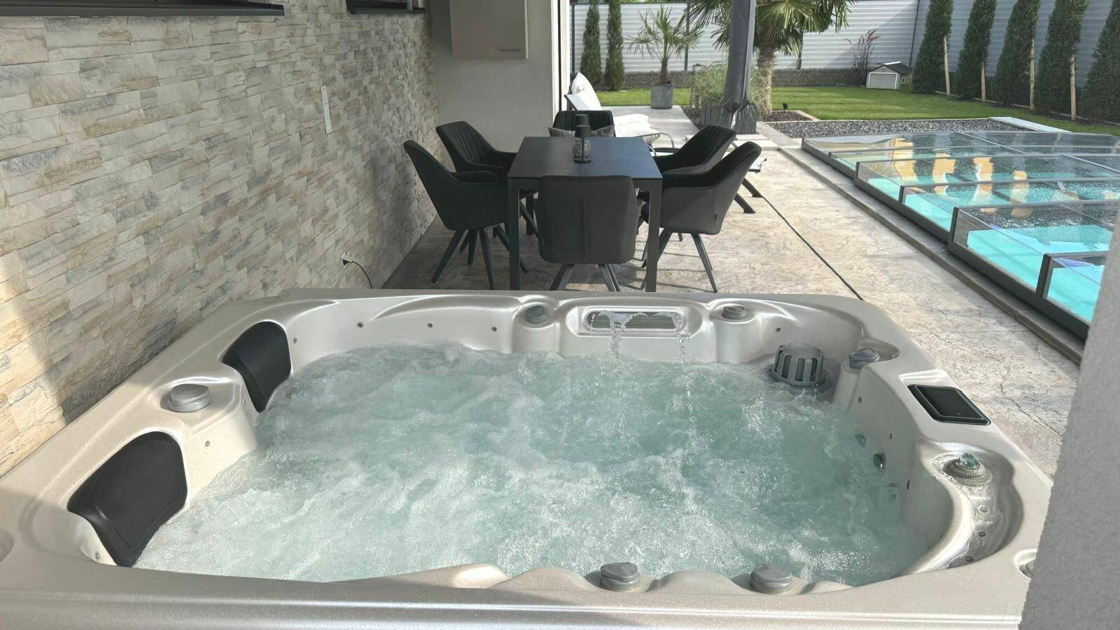 Gemütliche Terrasse mit Whirlpool, Essbereich und Steinwand, ideal zum Entspannen im Freien.
