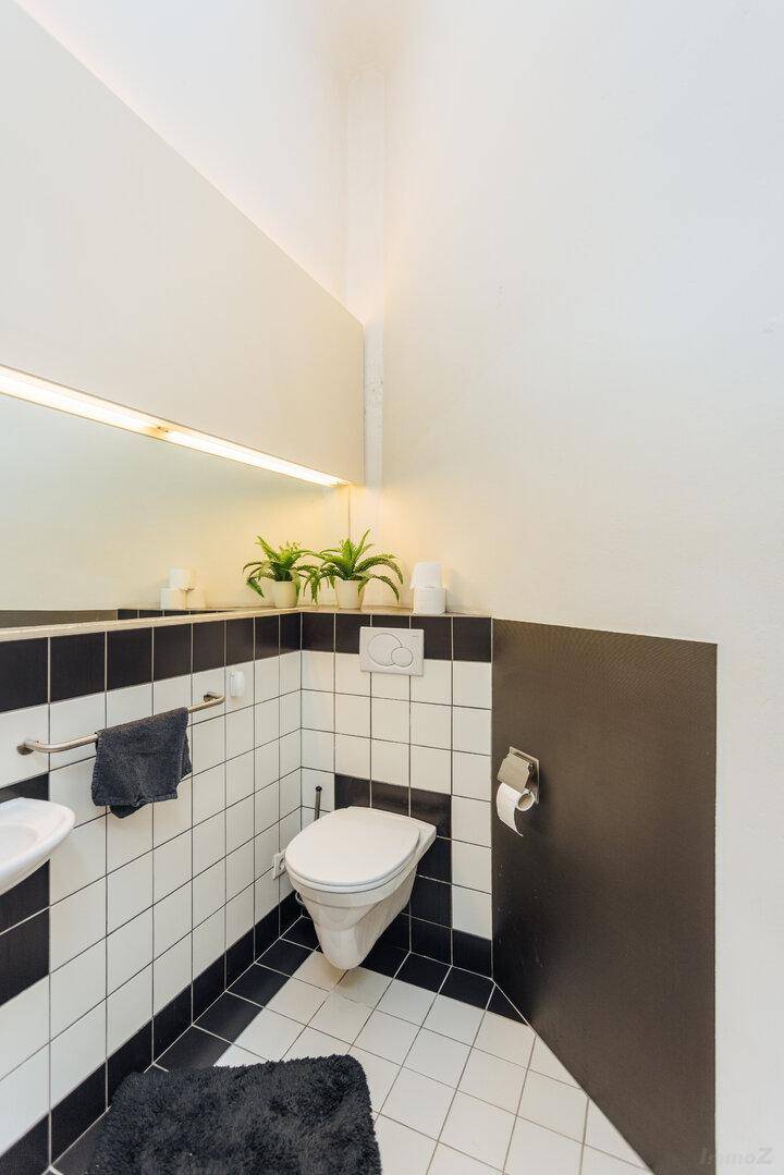 Gepflegte Toilette mit schwarz-weißen Fliesen, Wand-WC und Pflanzen als Dekoration.