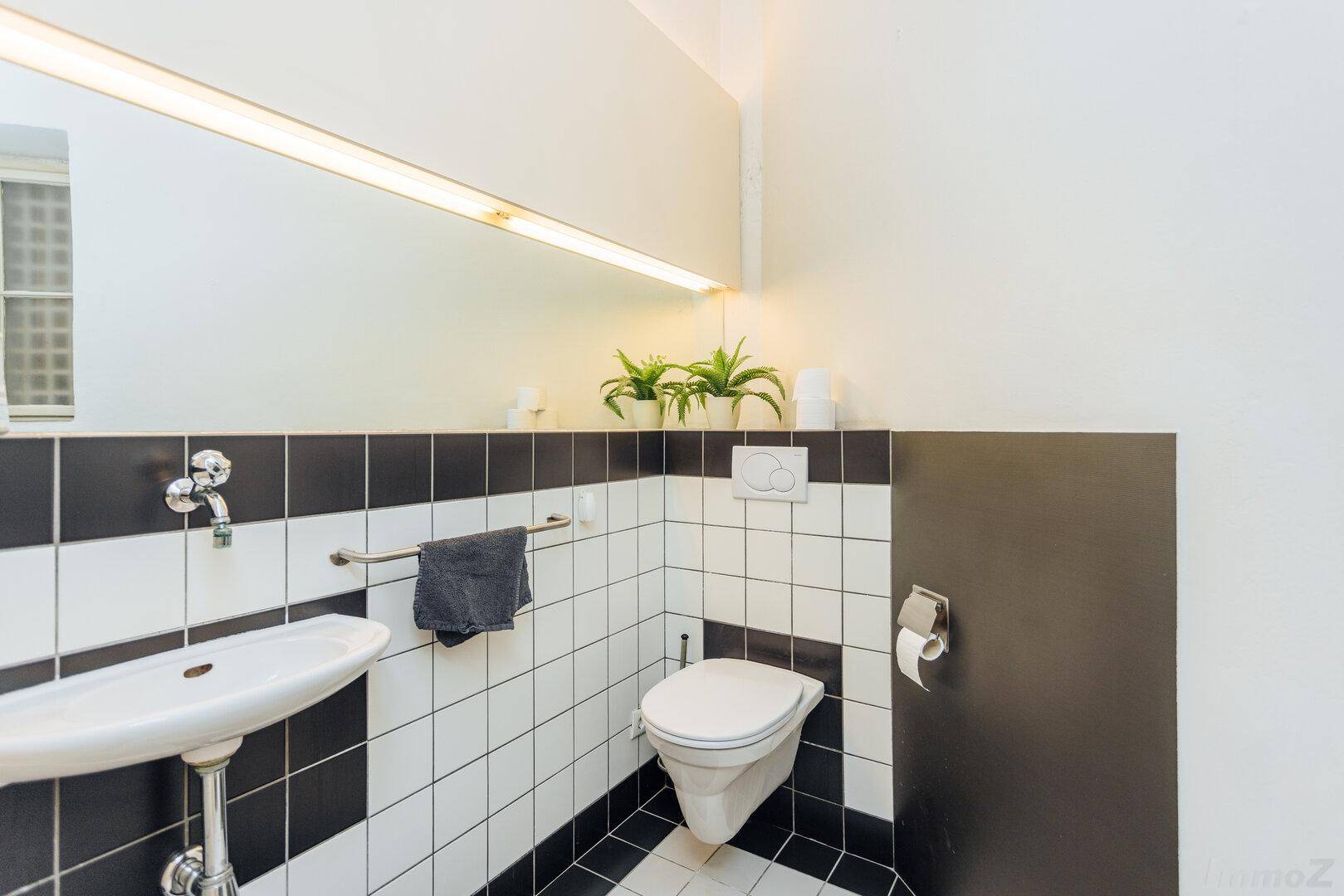 Modern geflieste Toilette in Schwarz-Weiß mit Waschbecken und Spiegel.
