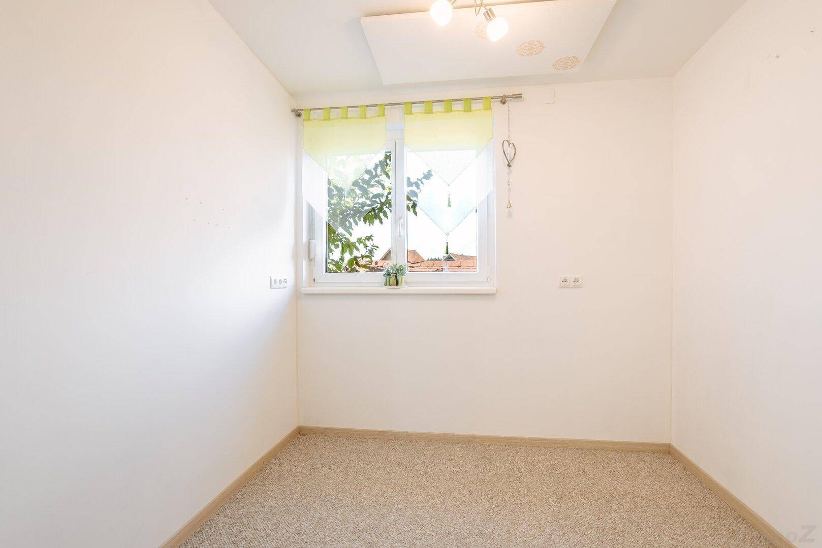 Leerer Raum mit hellem Teppichboden und einem Fenster, das viel Tageslicht hereinlässt.