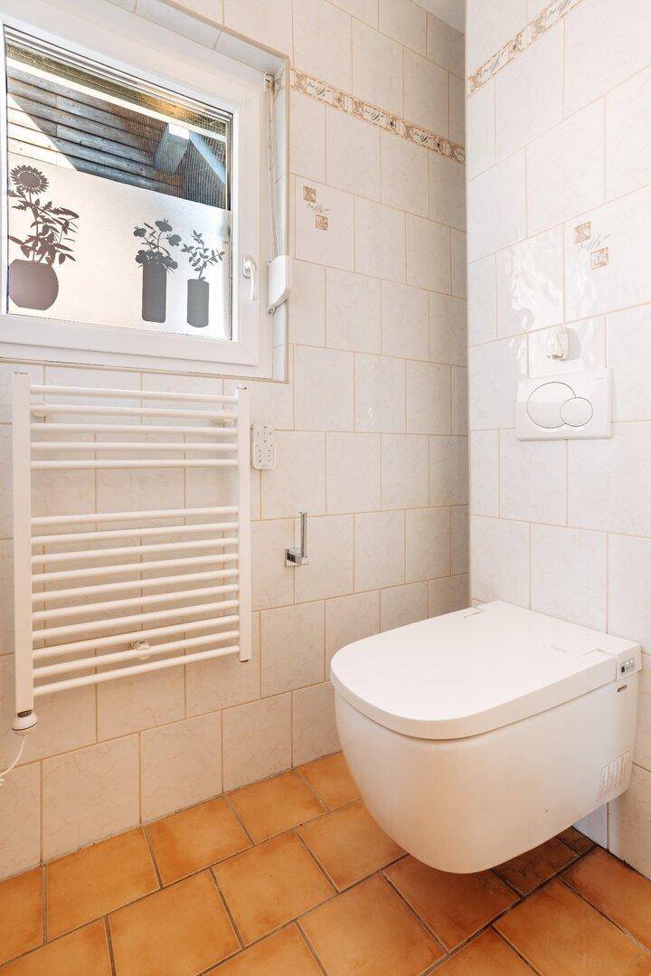 Badezimmer mit wandhängender Toilette, beheiztem Handtuchhalter und hellen Fliesen.