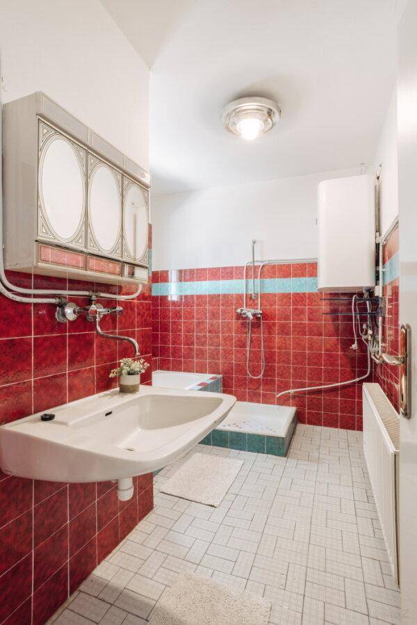 Badezimmer im Stil der 80er Jahre mit roten Fliesen, Dusche und Waschbecken.
