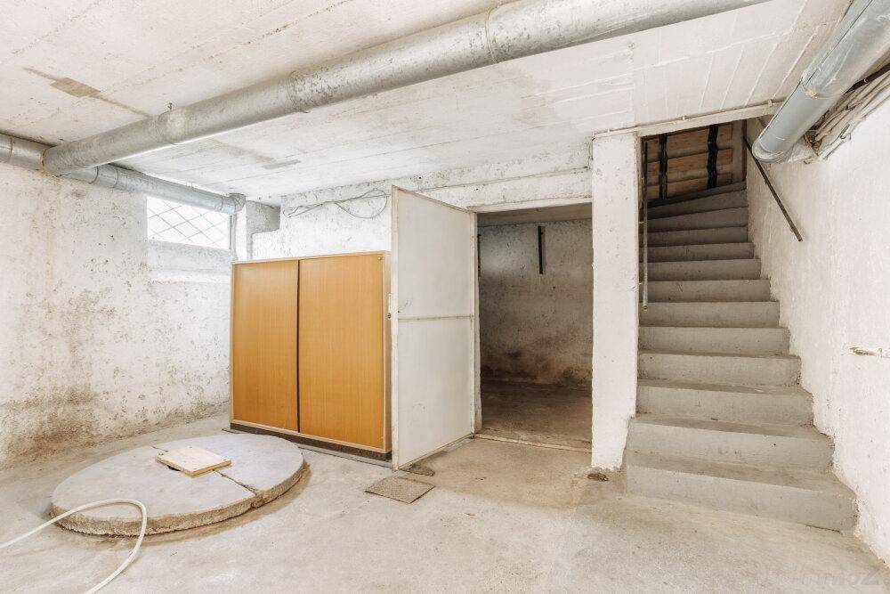Unfertiger Kellerraum mit Betontreppe, Lagerfläche und sichtbaren Rohren.