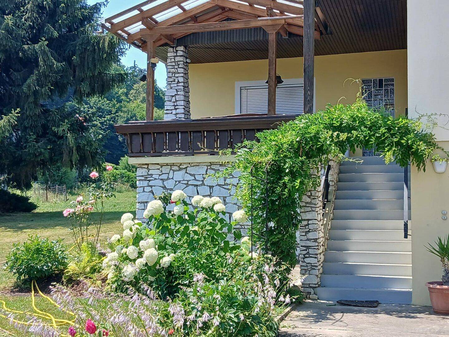 Eingangsbereich des Hauses mit überdachtem Balkon, Steintreppe und gepflegtem Vorgarten.