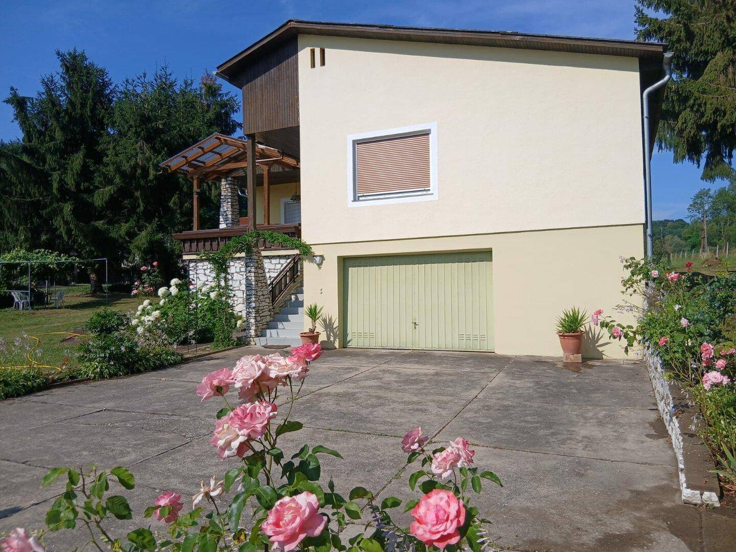 Ansicht des Hauses mit Garage, Zufahrt und blühenden Rosen im Vorgarten.
