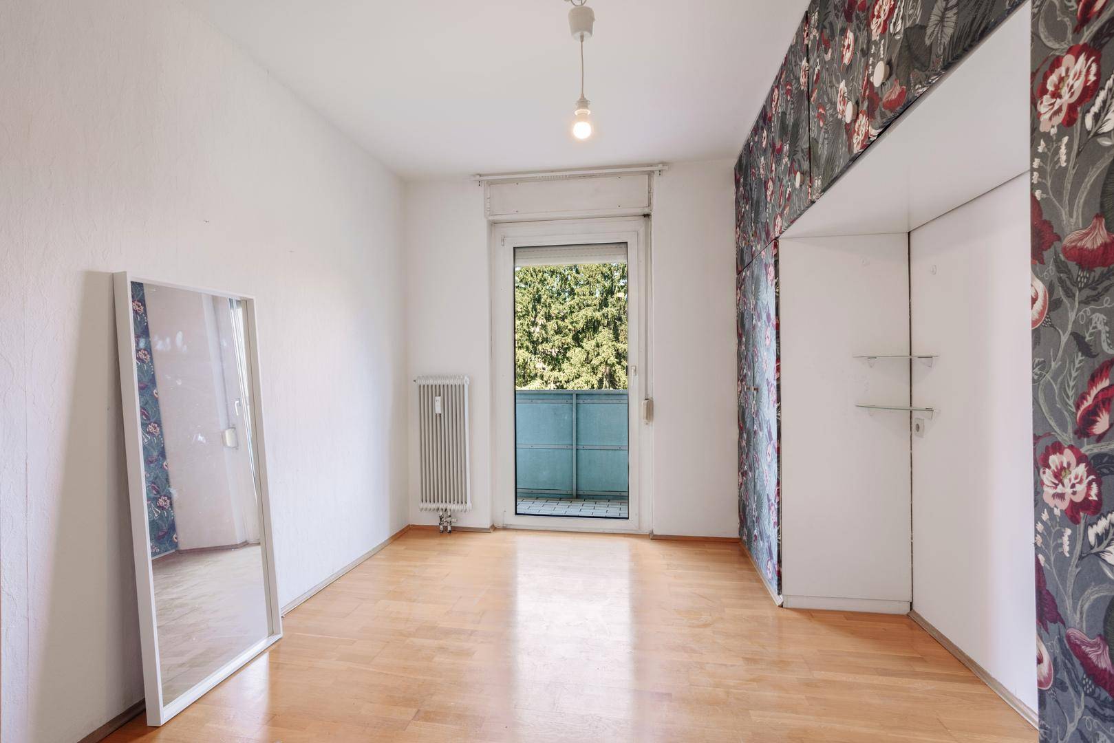 Schlafzimmer mit Parkettboden, floraler Tapete und Zugang zu einem kleinen Balkon.