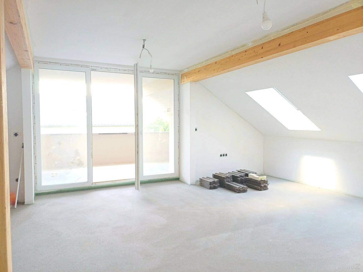 Heller, unfertiger Raum im Dachgeschoss mit sichtbaren Holzbalken, großen Schiebetüren und Dachfenstern.