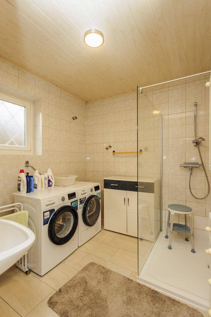 Badezimmer mit Duschkabine, Waschmaschine und Trockner, funktional und hell gefliest.