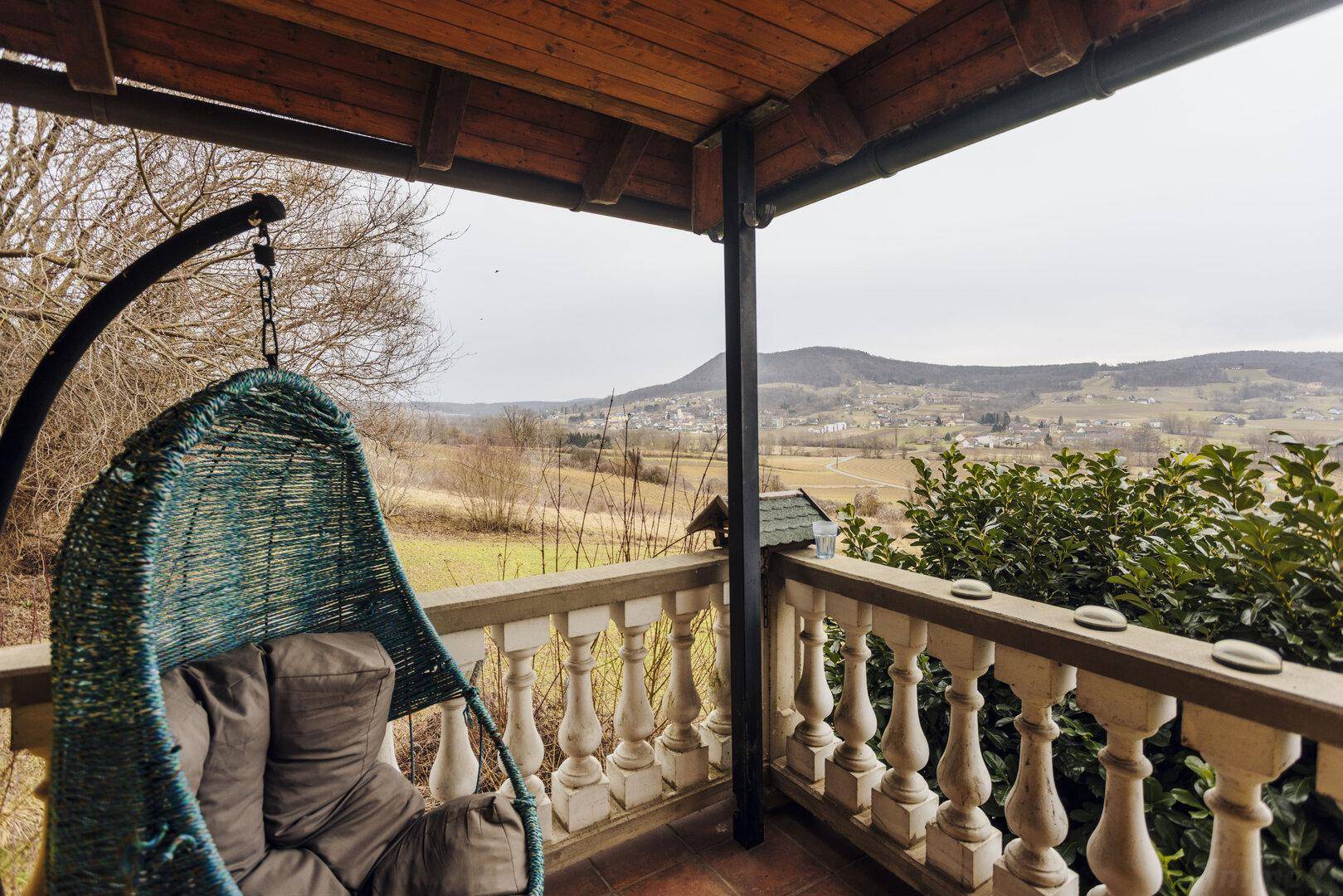 Überdachter Balkon mit Hängesessel und malerischem Blick auf die umliegende Landschaft.