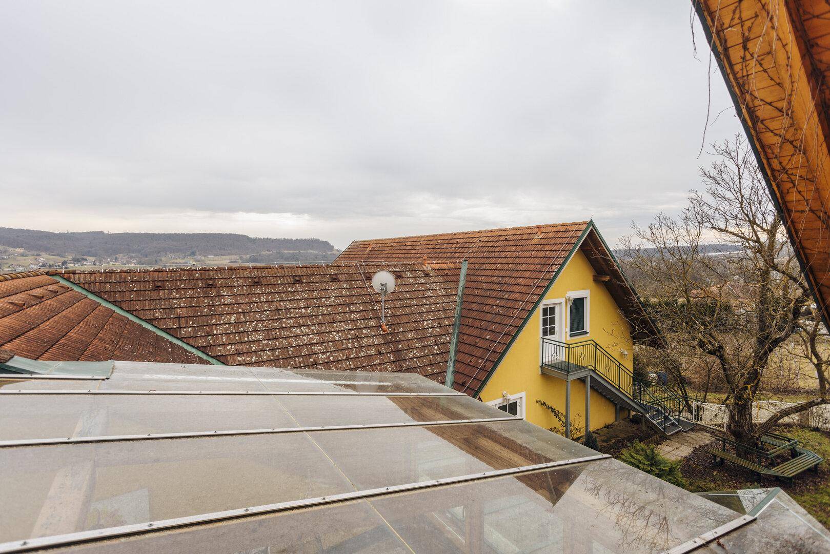 Dachansicht eines Hauses mit Ziegeldach und umliegender Landschaft unter bewölktem Himmel.