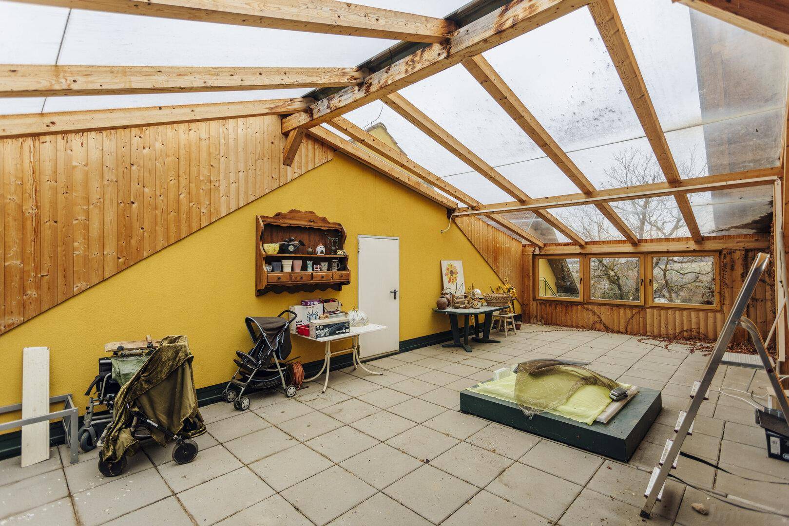 Geräumiger Wintergarten mit gelber Wand, Holzdecke und großen Fenstern, ideal für Pflanzen.