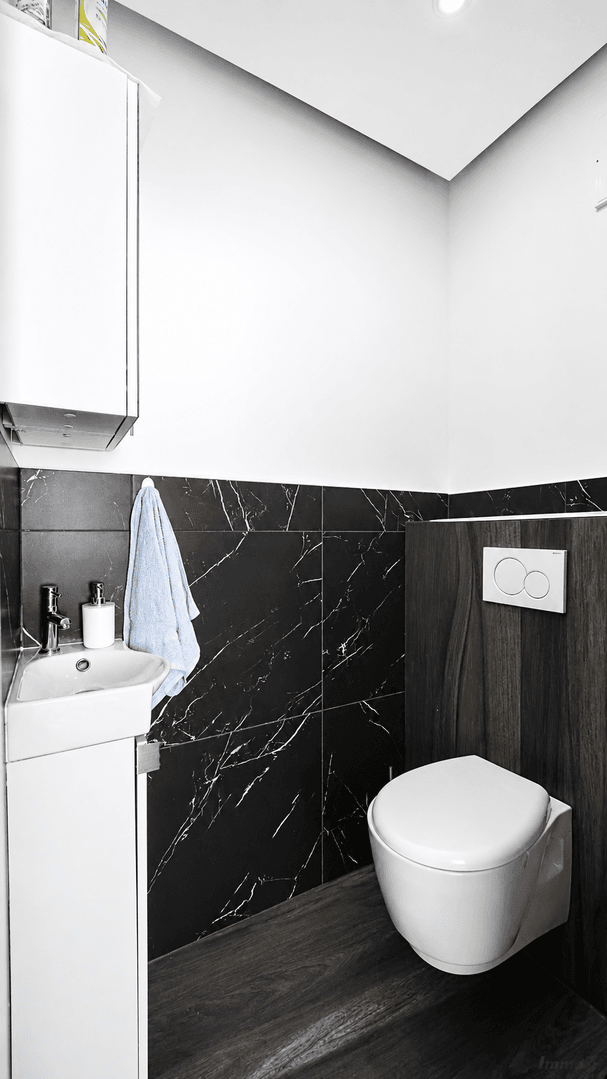 Modernes Gäste-WC mit dunklen Marmorfliesen, Wand-WC und kleinem Waschbecken.